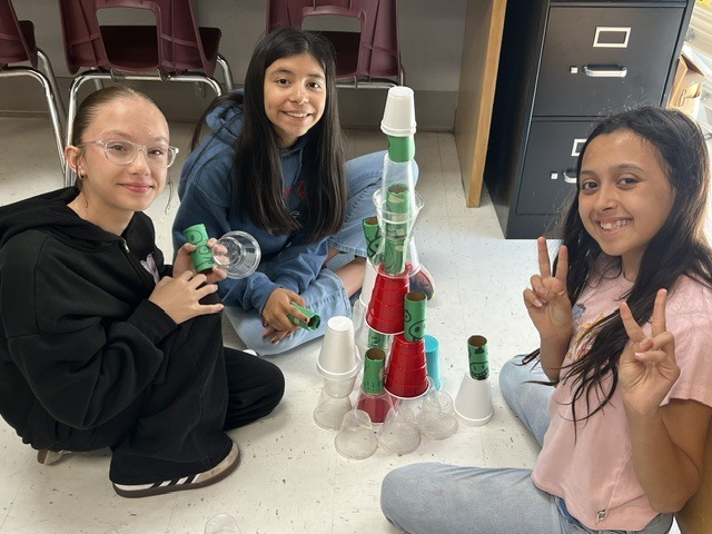 three girls  posing with their cups to knock down with their paper origami red bird