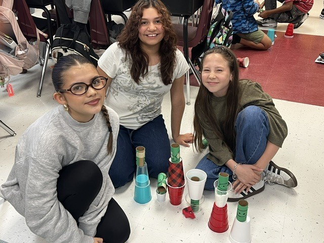 three girls posing with their cups to knock down with their paper origami red bird