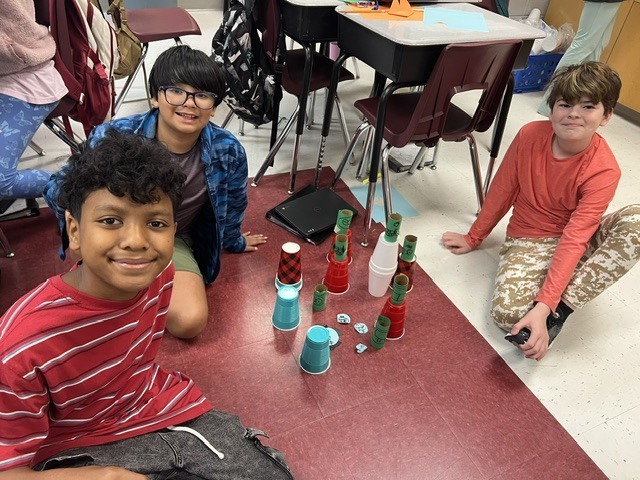 three boys posing with their cups to knock down with their paper origami red bird