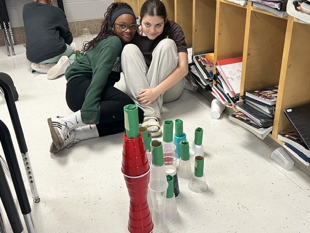 two students posing with their cups to knock down with their paper origami red bird