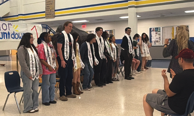 a mix of high school seniors stand inside their school after receiving their ib stoles for graduation