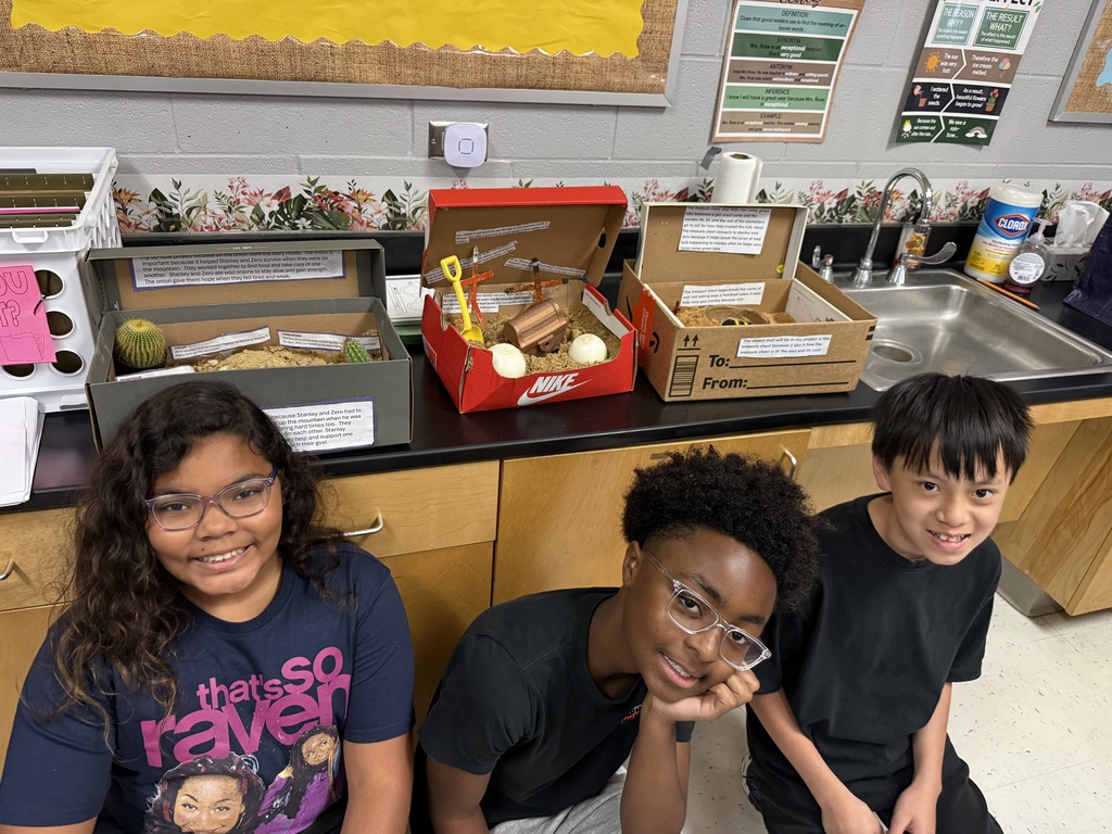 three students sitting in front of their shoe box models of scenes in the book Holes