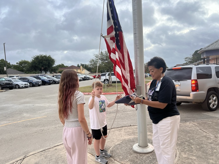 2 students and a teacher putting up the flag
