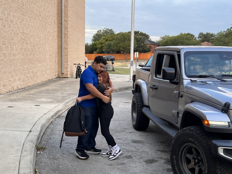 high schooler hugging his little sister in the car line