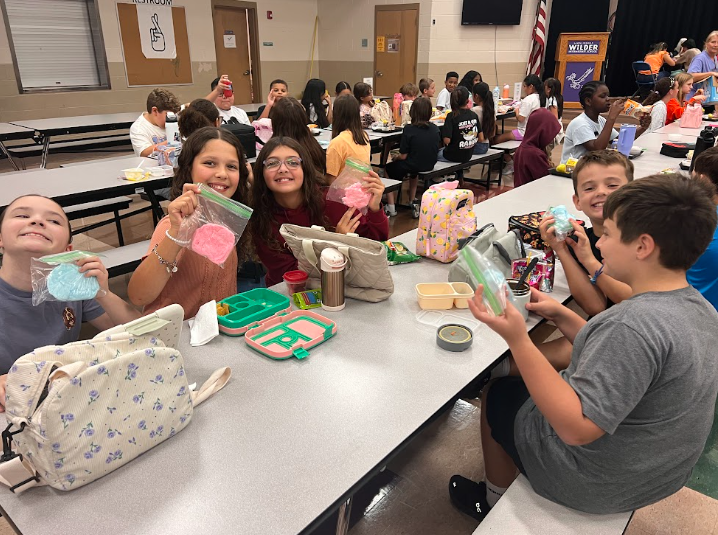 5th graders sitting at cafeteria table holding up their cotton candy.