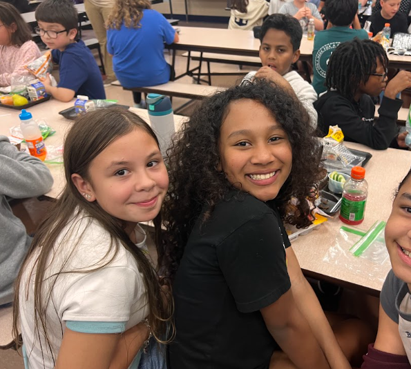 2 girls sitting in the cafeteria smiling at camera