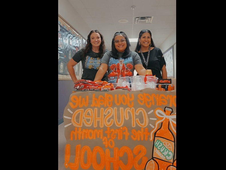 three staff members standing behind a cart that says, Orange you glad we CRUSHED the first month of school.