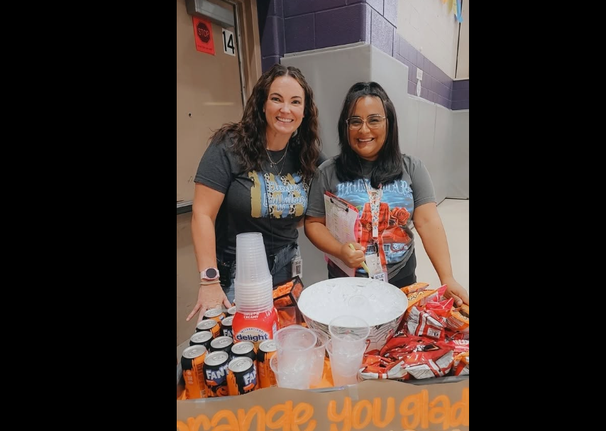 Mrs. Dean and Mrs. Trevino pushing a cart full of orange snacks