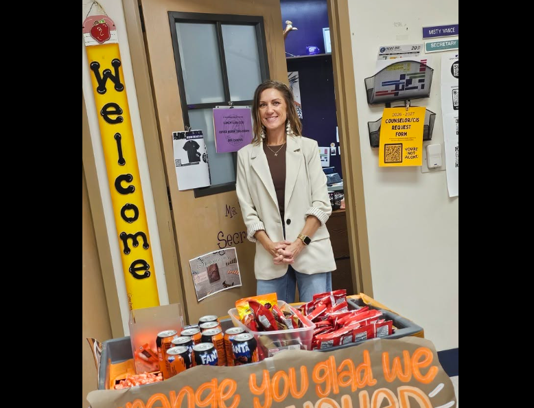 Mrs. Vance standing by her door near a cart of orange snacks