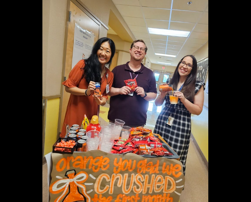 two female teachers and one male teacher holding up the orange snack that they chose from the cart