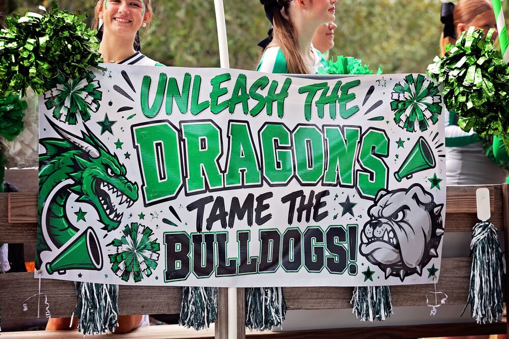 Spirit banner reading Unleash the Dragons Tame the Bulldogs held by cheerleaders.
