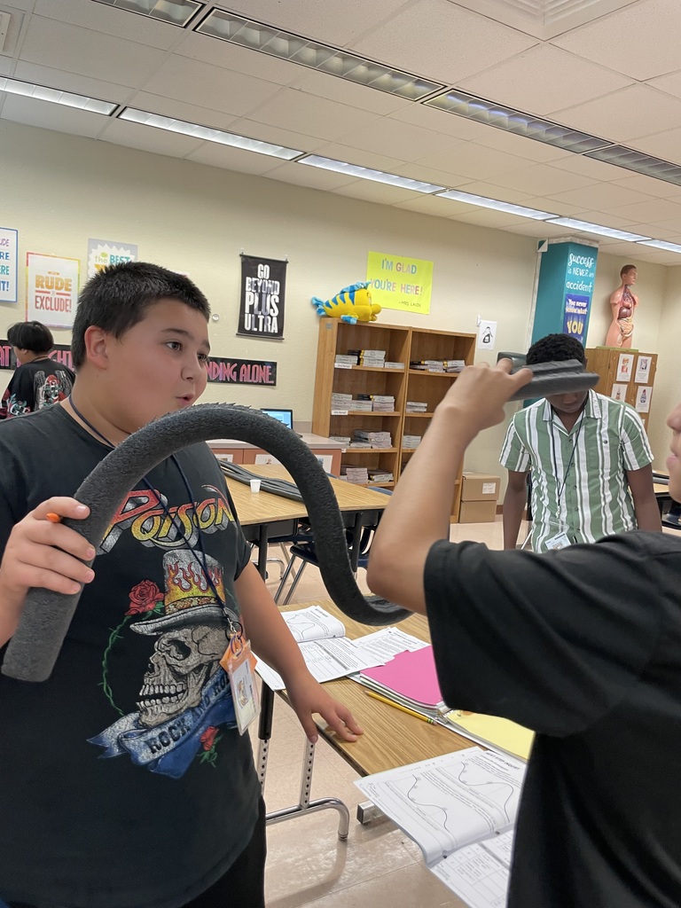 A student holds a foam ramp while talking with a partner during a science experiment.