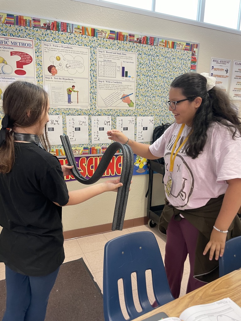 Two students stand and hold a foam ramp together in front of a science poster display.