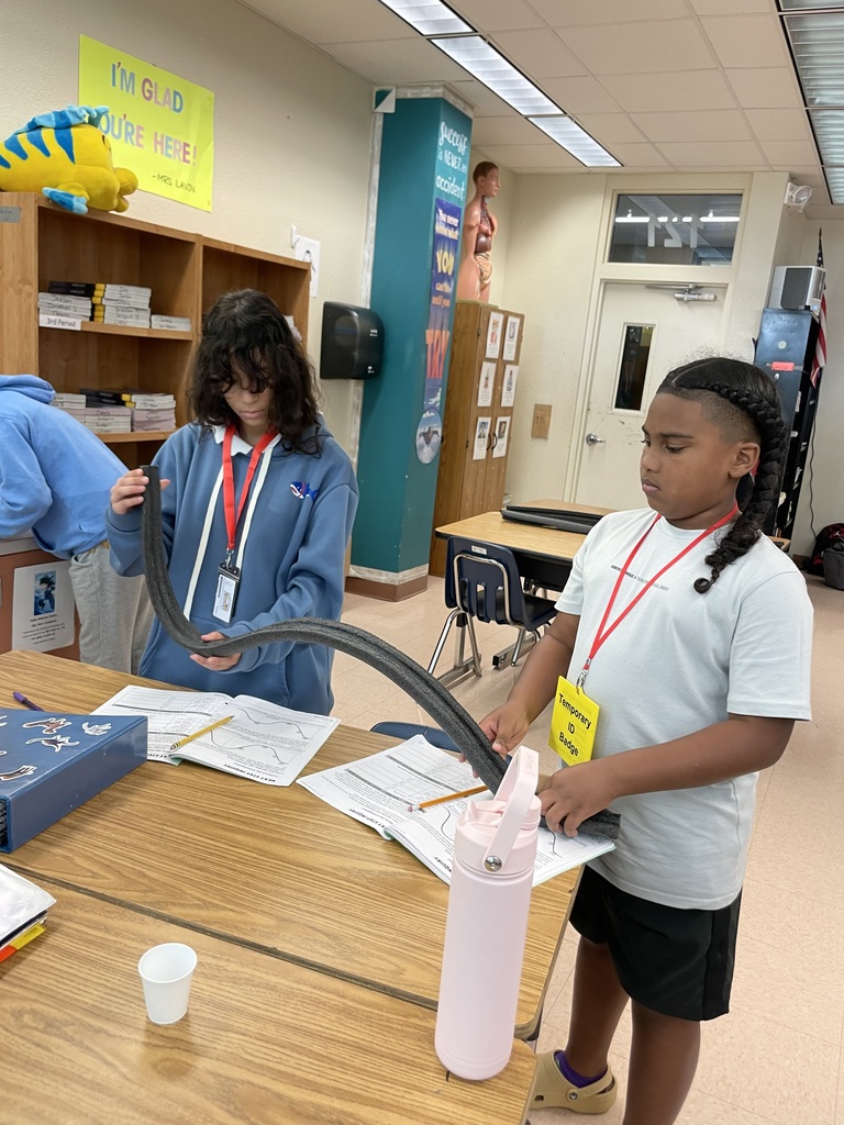 Two students at a table hold a curved foam ramp while working on a science lab.