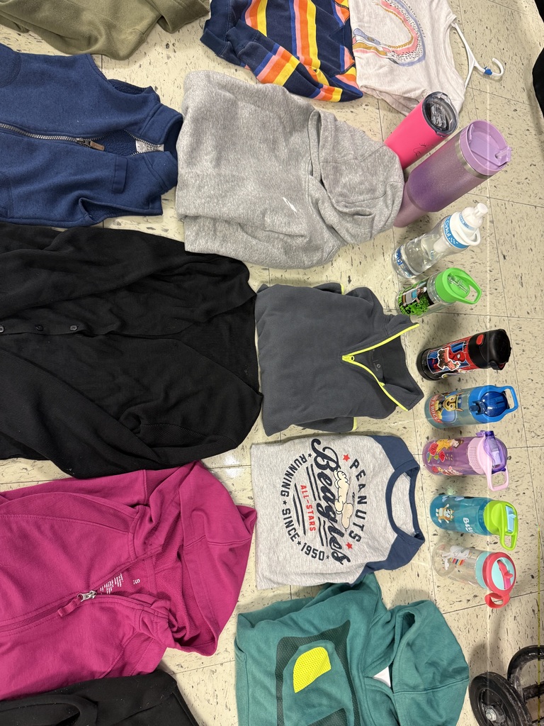  A variety of lost-and-found items, including jackets, water bottles, and lunchboxes, are laid out on a beige tile floor. The items are spread out in groups, with many colorful jackets and several water bottles with popular cartoon characters.