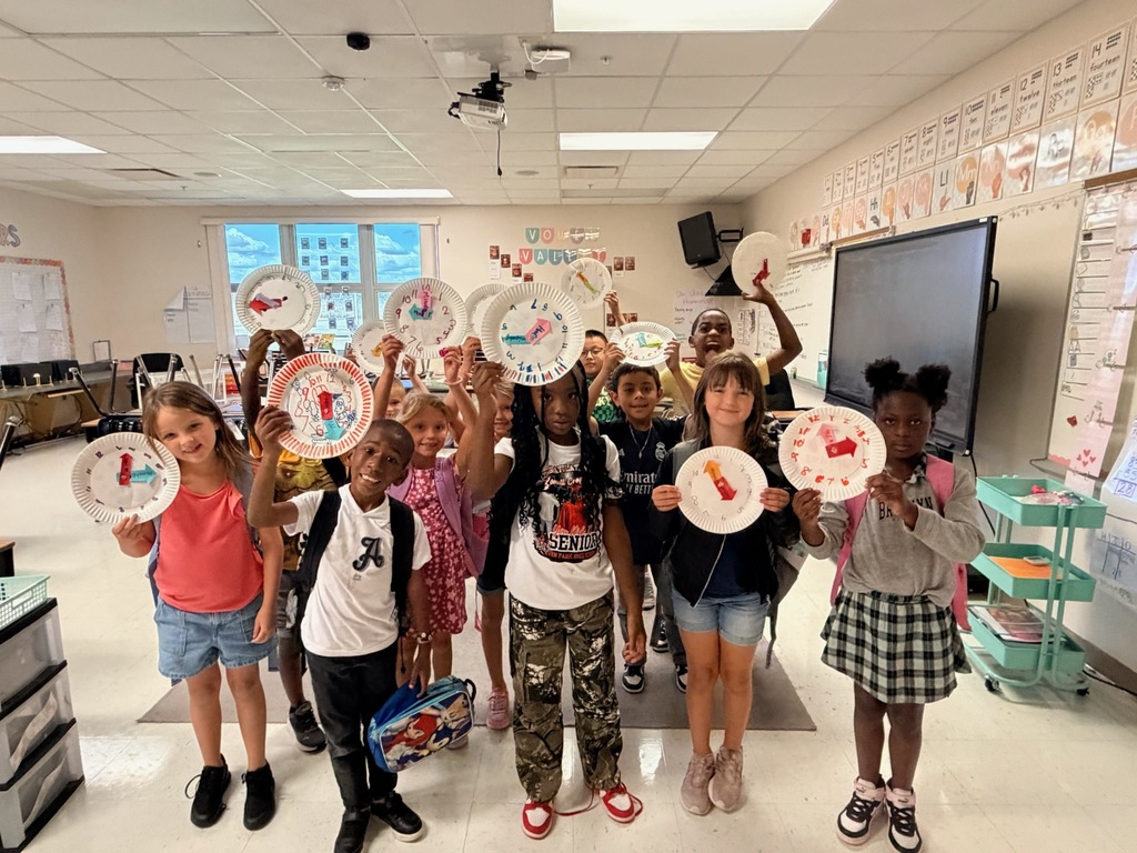 MES primary class students holding up paper plate clocks they have made to help with telling time.