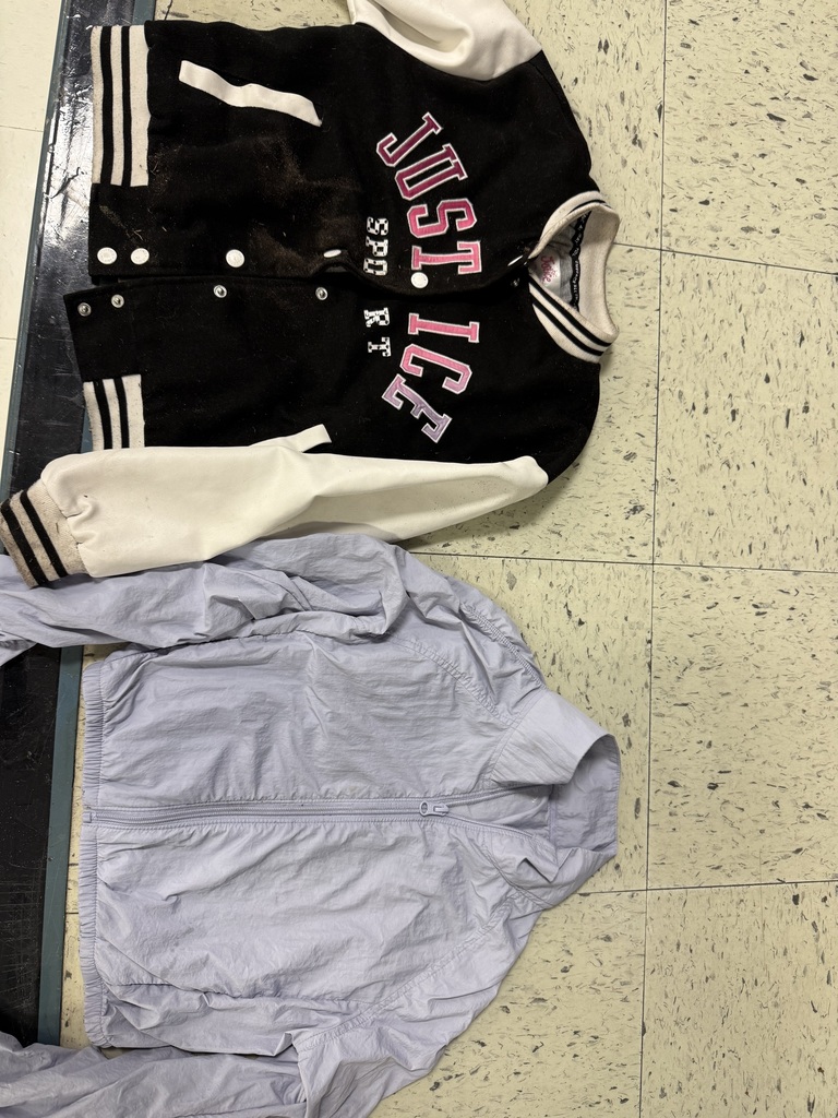 Two jackets: a black and white varsity-style jacket with "Justice" in pink lettering, and a light lavender zip-up windbreaker.