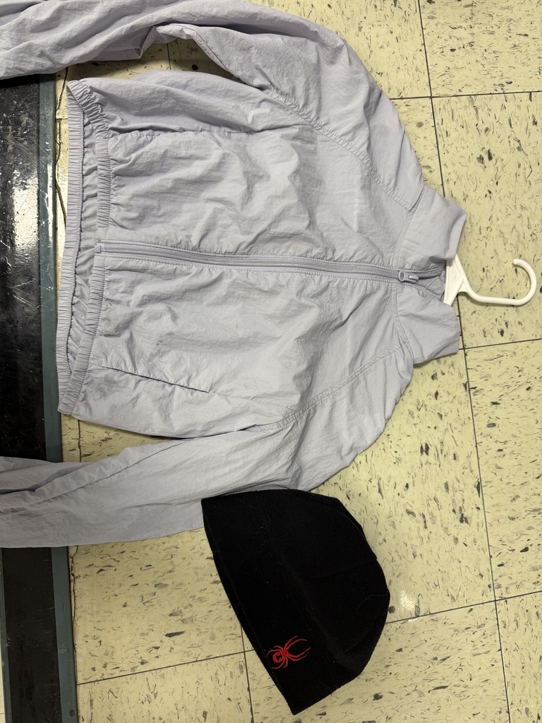 A light lavender zip-up windbreaker and a black knit beanie.