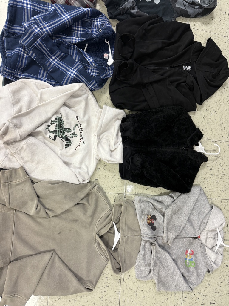 A group of sweatshirts and zip-up jackets in dark colors, white, and tan, including a blue plaid flannel and a gray Mickey Mouse hoodie.