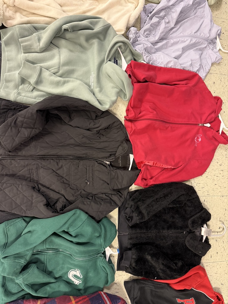 A collection of jackets and sweatshirts are piled on a tiled floor. Colors include light sage green, black quilted, dark green, red, black fuzzy, cream, and a crumpled lavender windbreaker.