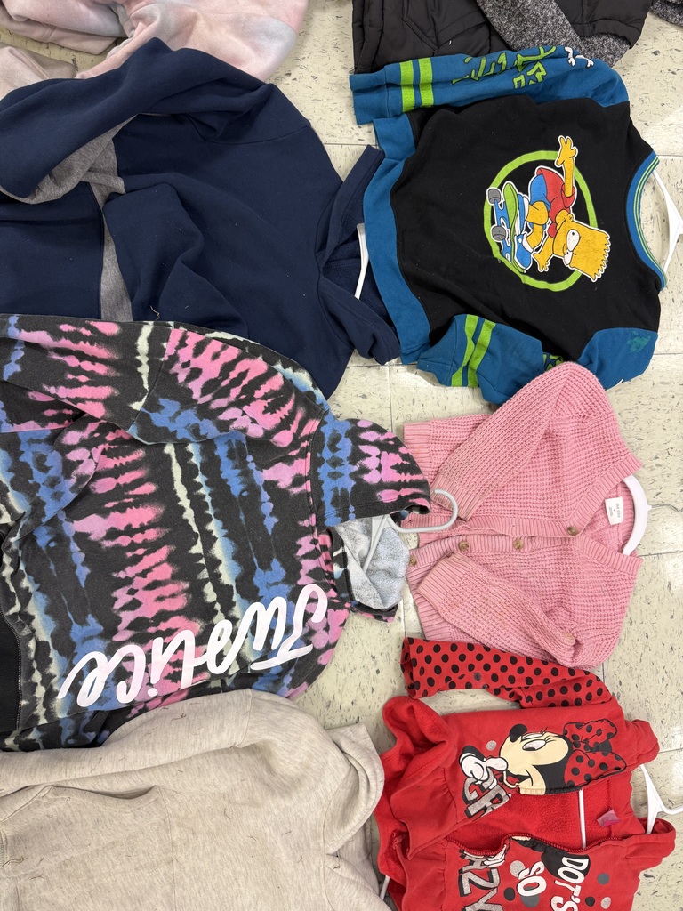 A group of children's garments including a black Bart Simpson sweatshirt, a black and pink tie-dye 'Justice' hoodie, a pink knit cardigan, a red polka-dot Minnie Mouse hoodie, and a navy sweatshirt.
