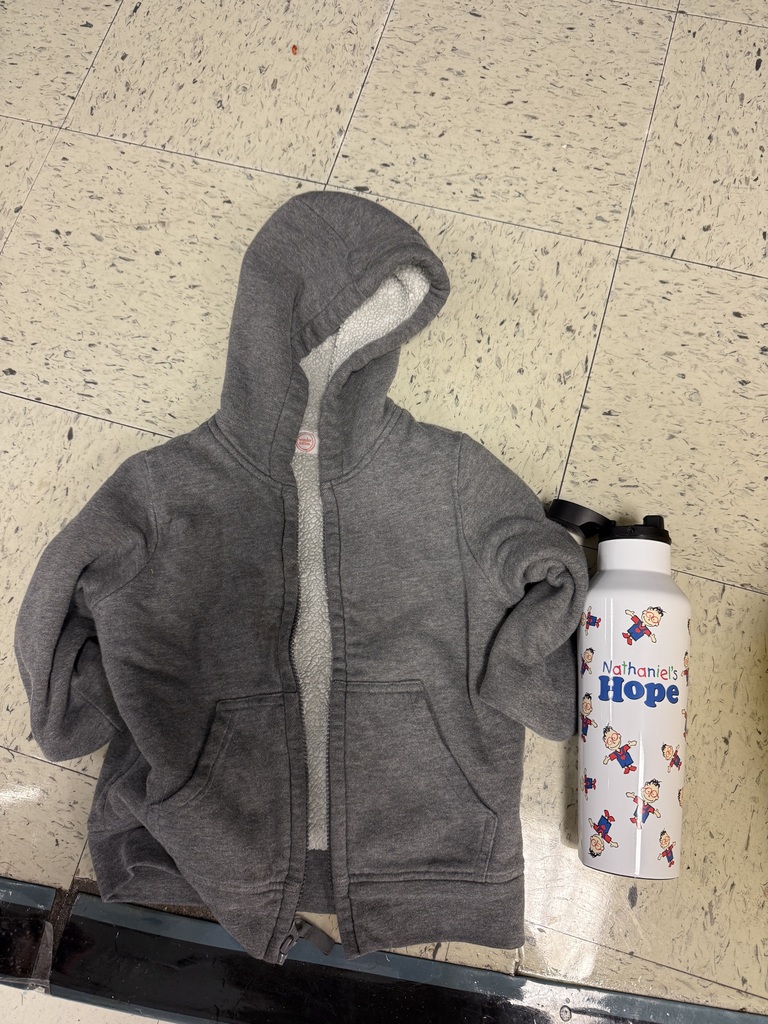A small, gray fleece-lined children's zipper hoodie with the hood up is lying on a tiled floor next to a white water bottle featuring the "Nathaniel's Hope" logo with small cartoon boys.