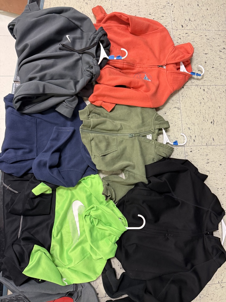A pile of zip-up hoodies and jackets, featuring a dark gray Nike fleece, a bright orange hoodie, a navy blue fleece, an olive green hoodie, a neon green Nike athletic shirt, and a black jacket.