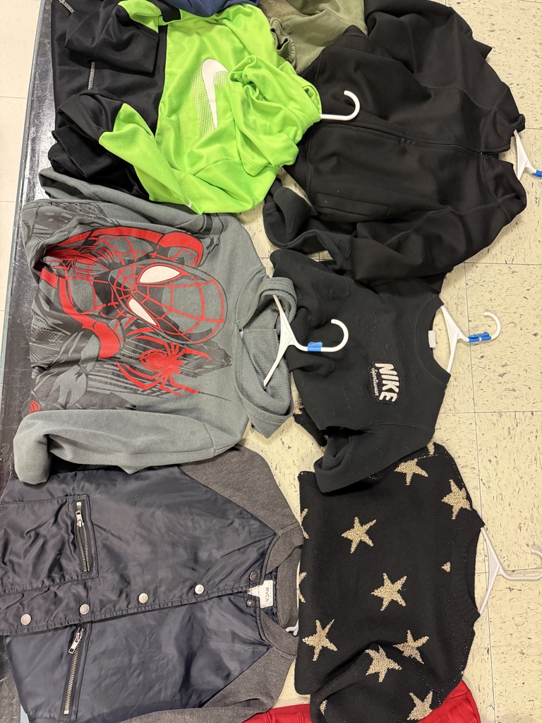 A collection of children's jackets and sweaters laid out, including a neon green Nike shirt, a gray Spider-Man hoodie, a black Nike sweater, a dark blue bomber jacket, and a black sweater with gold stars.