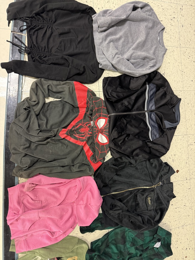 An assortment of children's jackets on a tiled floor, featuring a pink bear varsity jacket, a black Champion hoodie, a Spider-Man hoodie, a black Calvin Klein zip-up, and several patterned fleece jackets.