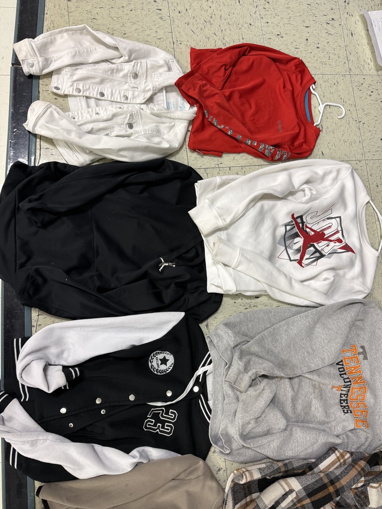 Several items of apparel including a white denim jacket, a red long-sleeve shirt, a white Jordan sweatshirt, a black and white varsity jacket with "23," and a grey Tennessee Volunteers sweatshirt.