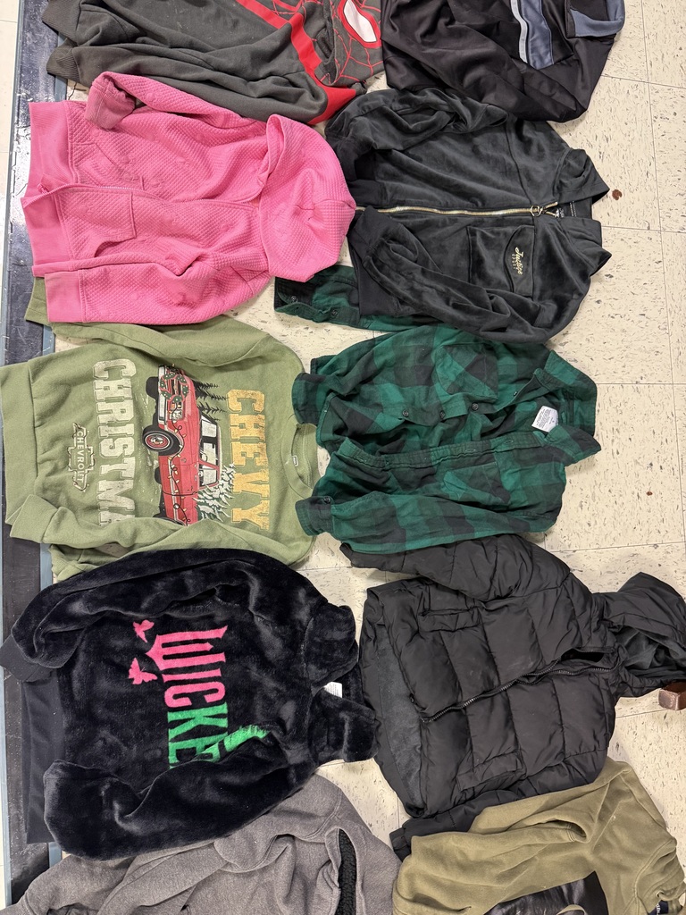 A close-up of clothing items including an olive "Chevy Christmas" sweatshirt, a black fuzzy jacket with "Wicked" in pink text, a green plaid shirt, and a black puffer jacket.