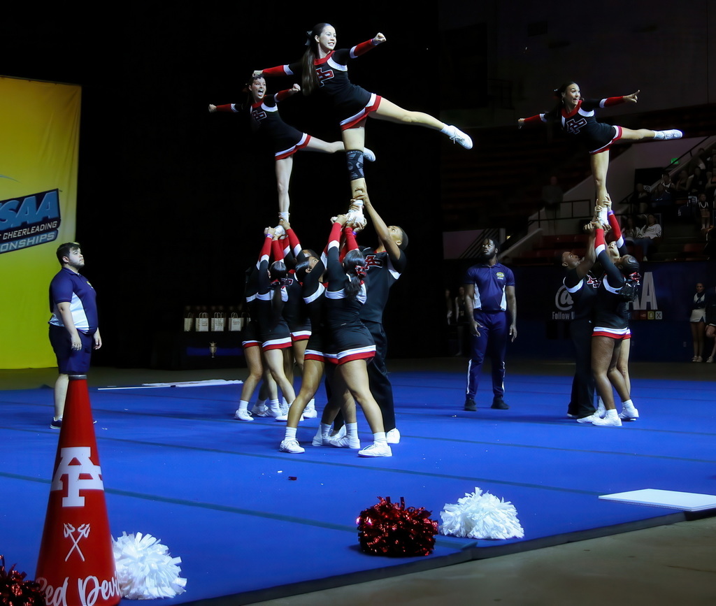 Cheer team preforms an arial maneuver with a base and a cheerleader at the top.