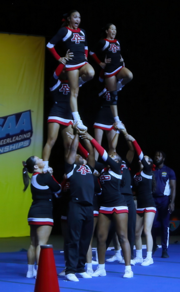 Cheer team preforms an arial maneuver with a base and a cheerleader at the top.