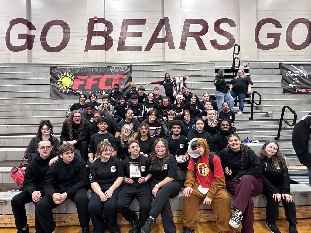 A large, energetic group of students poses on gym bleachers under a "GO BEARS GO" sign. Many cheer with raised fists while three students in the front row proudly hold a competition plaque. One student wears a red and brown character onesie. A banner for "FFCC" hangs behind them.