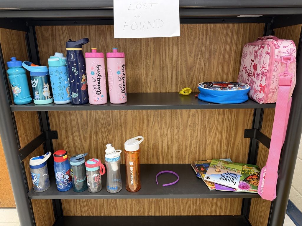 A "Lost and Found" shelf containing eleven water bottles of various colors and designs, a Spiderman lunch container, a pink bow-patterned bag, a purple headband, and several children's books.