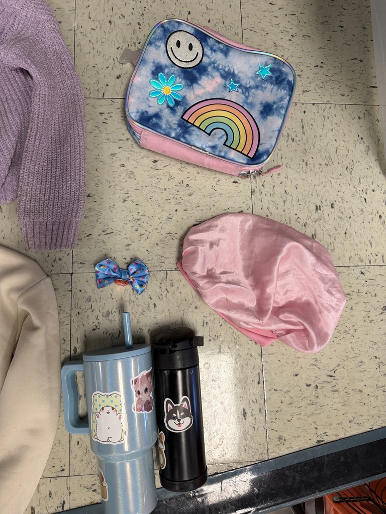 Five accessories and personal items. Features a blue tie-dye lunchbox with a rainbow and smiley face, a pink satin hair bonnet, a blue patterned bow, a glittery blue tumbler, and a black water bottle with stickers.