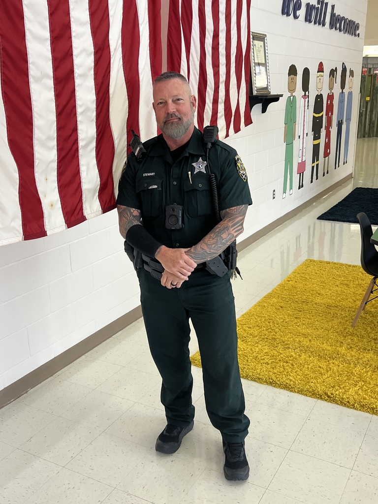 Standing picture of Deputy Stewart in the Front lobby of MES in front of the USA Flags and painted mural in the back. 