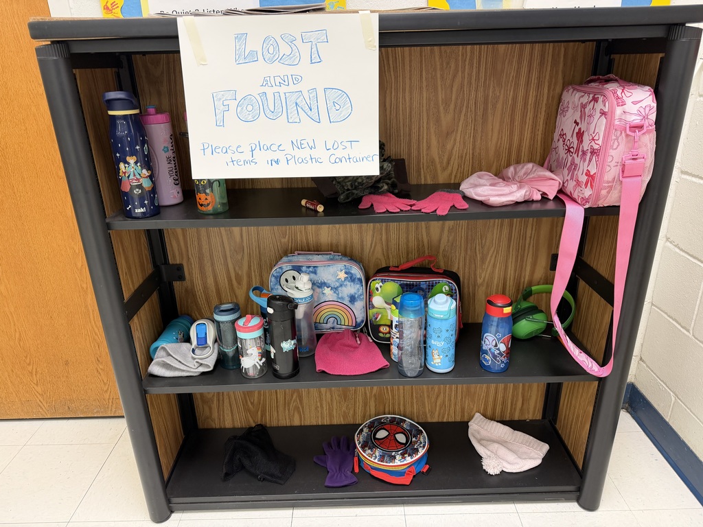 A black three-shelf unit labeled "Lost and Found." It contains various water bottles, colorful lunch boxes (including Spiderman and rainbow themes), several pairs of gloves, knit beanies, and a pair of green headphones.