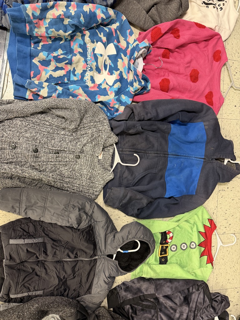 A collection of children's apparel featuring a blue "Under Armour" camo hoodie, a bright pink sweater with red hearts, a grey button-down cardigan, a navy and royal blue zip-up jacket, a black and grey puffer jacket, and a lime green "Elf" costume shirt.