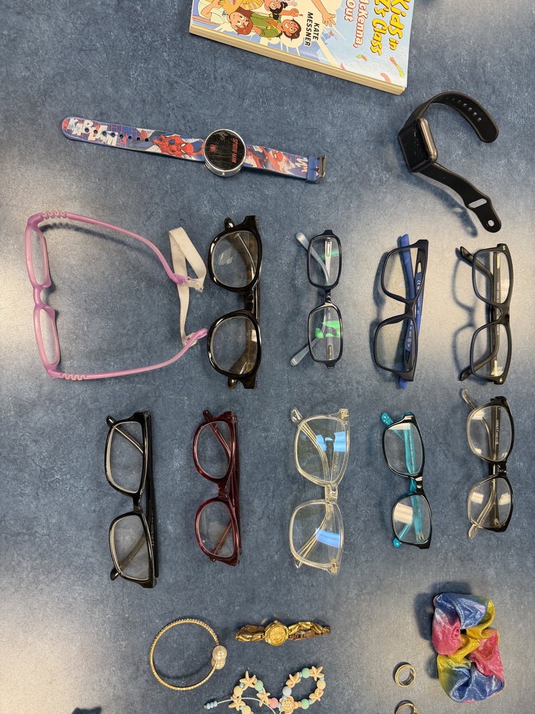 Ten pairs of eyeglasses in various colors (black, purple, red, clear, teal), a Spider-Man watch, a black smartwatch, a gold watch, and assorted jewelry laid out on a blue surface.