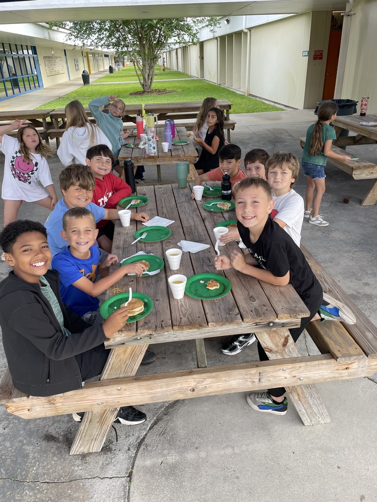 students eating pancakes and sitting at a picnic table smiling