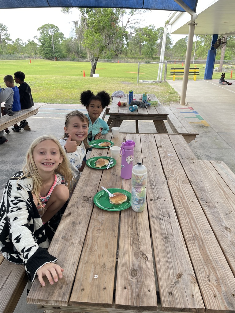 students eating pancakes and sitting at a picnic table smiling