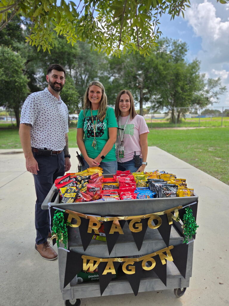 Picture of Mr. Hoffner, Mrs. Floyd and Mrs. Weldy standing with the Dragon Wagon full of treats.