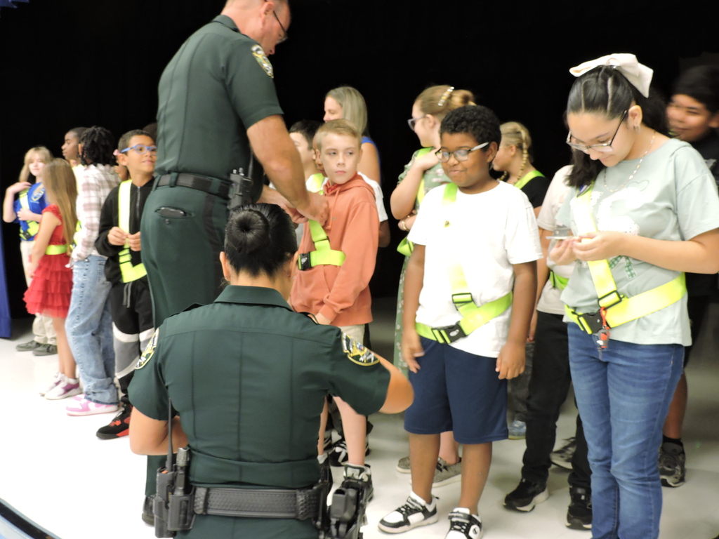 Sherrif Paul Blackman pins a safety patrol student and Lieutenant Gunn hands out Sheriff's Department challenge coins to other safety patrolers.