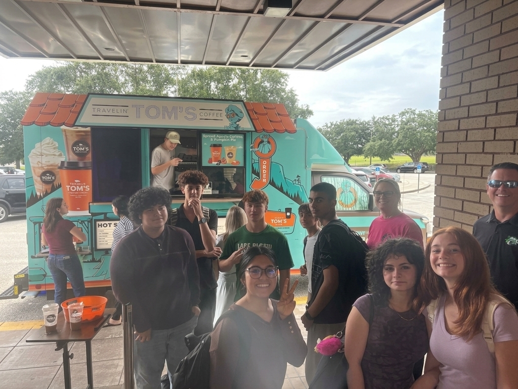 A student gives a peace sign as a group of students and staff pose by a coffee truck.