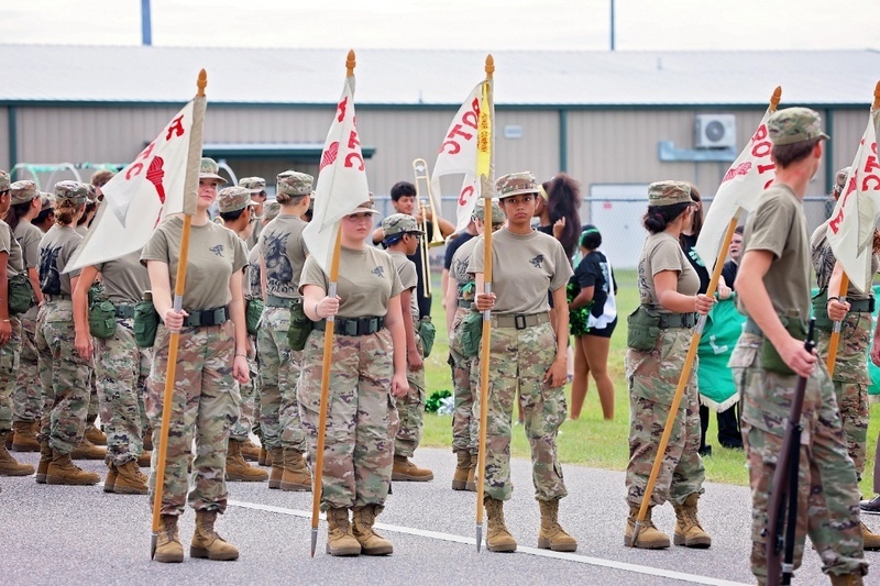 JROTC cadets standing in formation holding flags on a parade route.