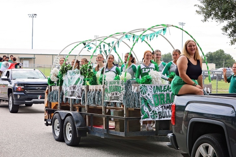 Parade float carrying cheerleaders decorated with green arches and Dragon banners.