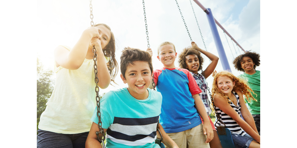 students sitting on and standing by swings