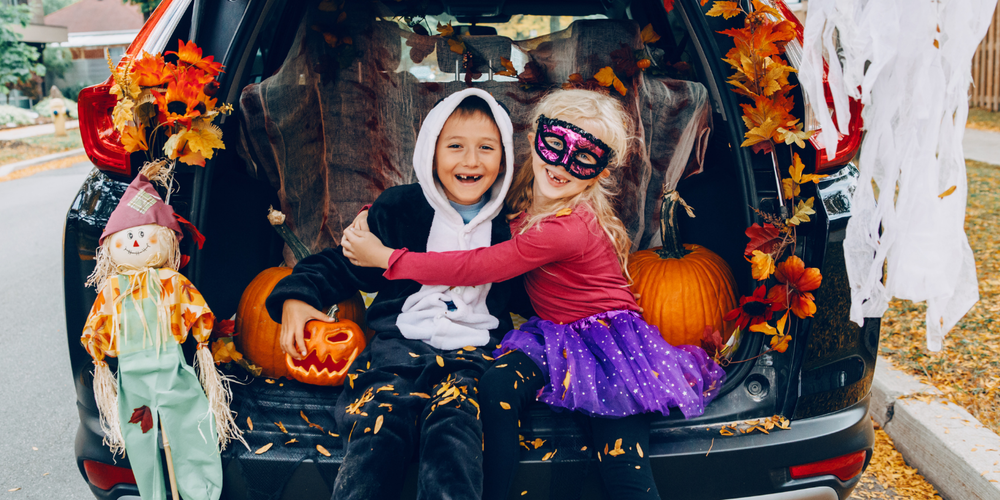 kids dressed in costumes sitting in a car trunk decorated with fall decor