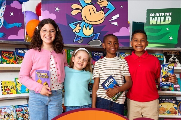 Photo of 4 students holding books and standing in front of book fair carts